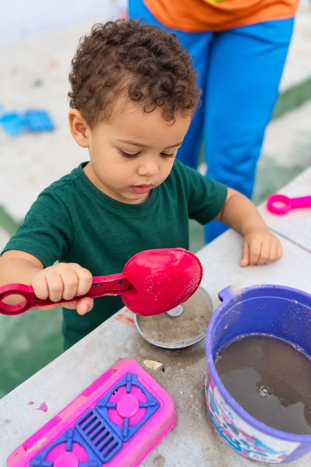 Criança brincando com terra, água e potes coloridos no quintal da escola